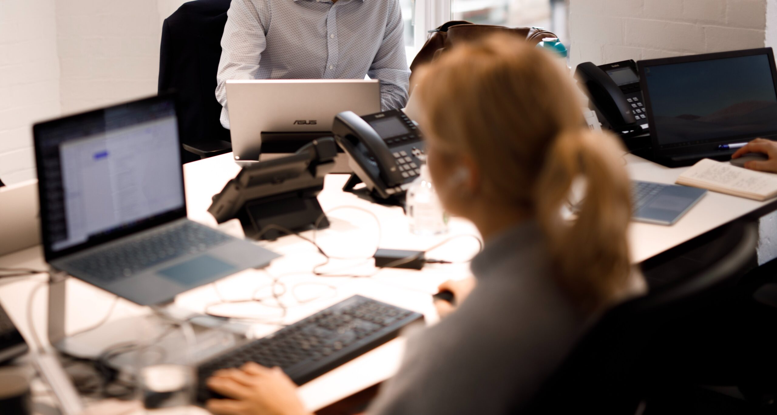 Person typing at a desk in the office, facing a colleague working on a laptop