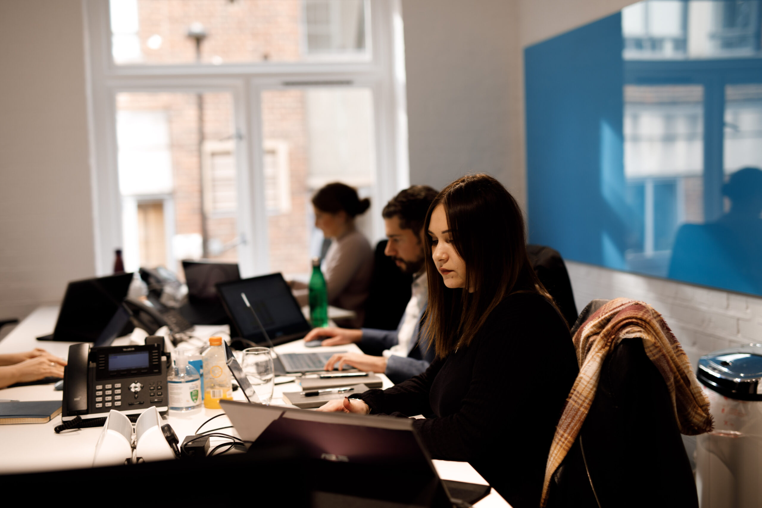 Team members working at laptops along a shared desk in a bright office at The Media People