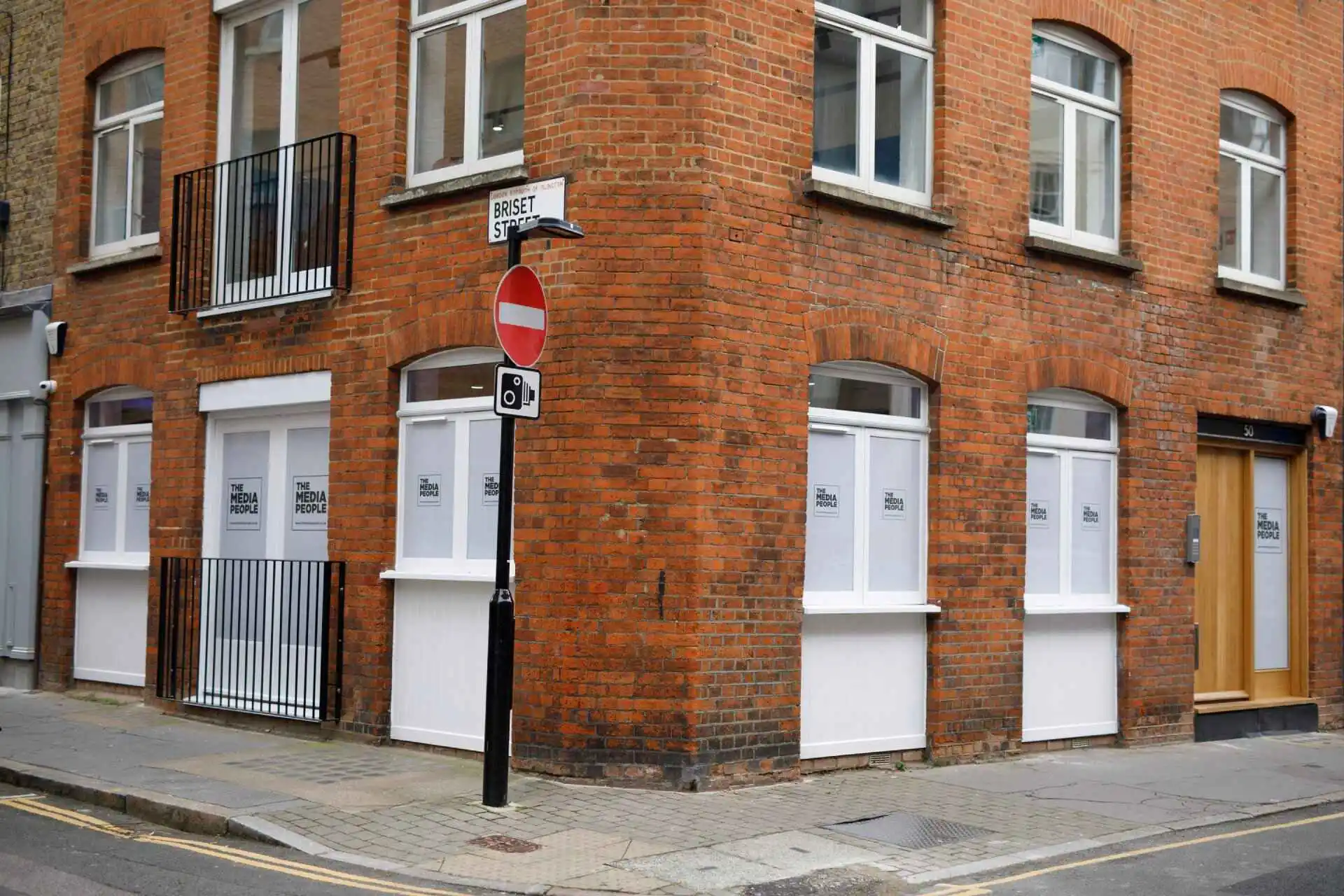 Corner of The Media People's red-brick office on Britton Street, with logos in the ground-floor windows