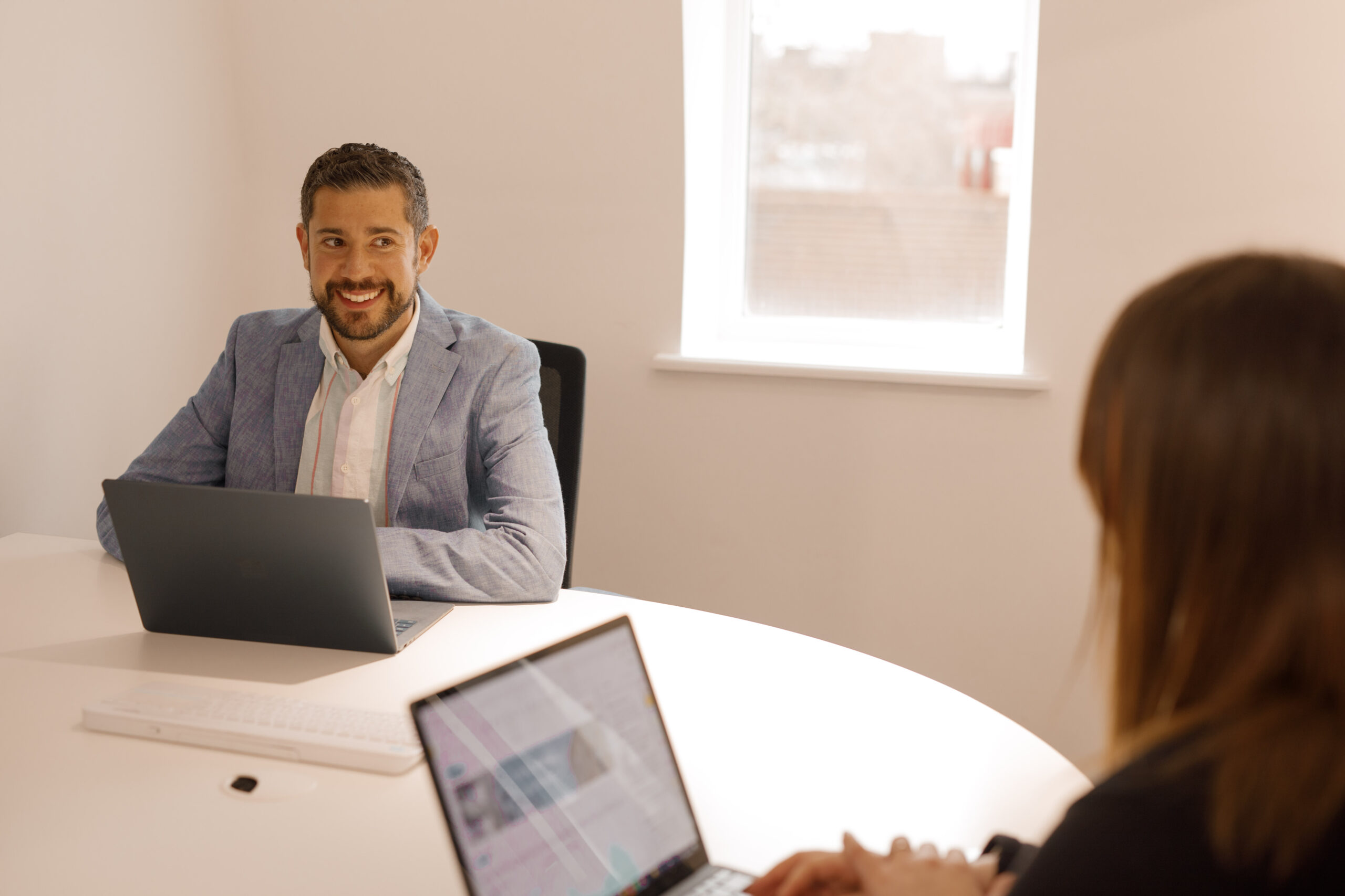 Two colleagues with laptops at a round white table in a meeting room at The Media People