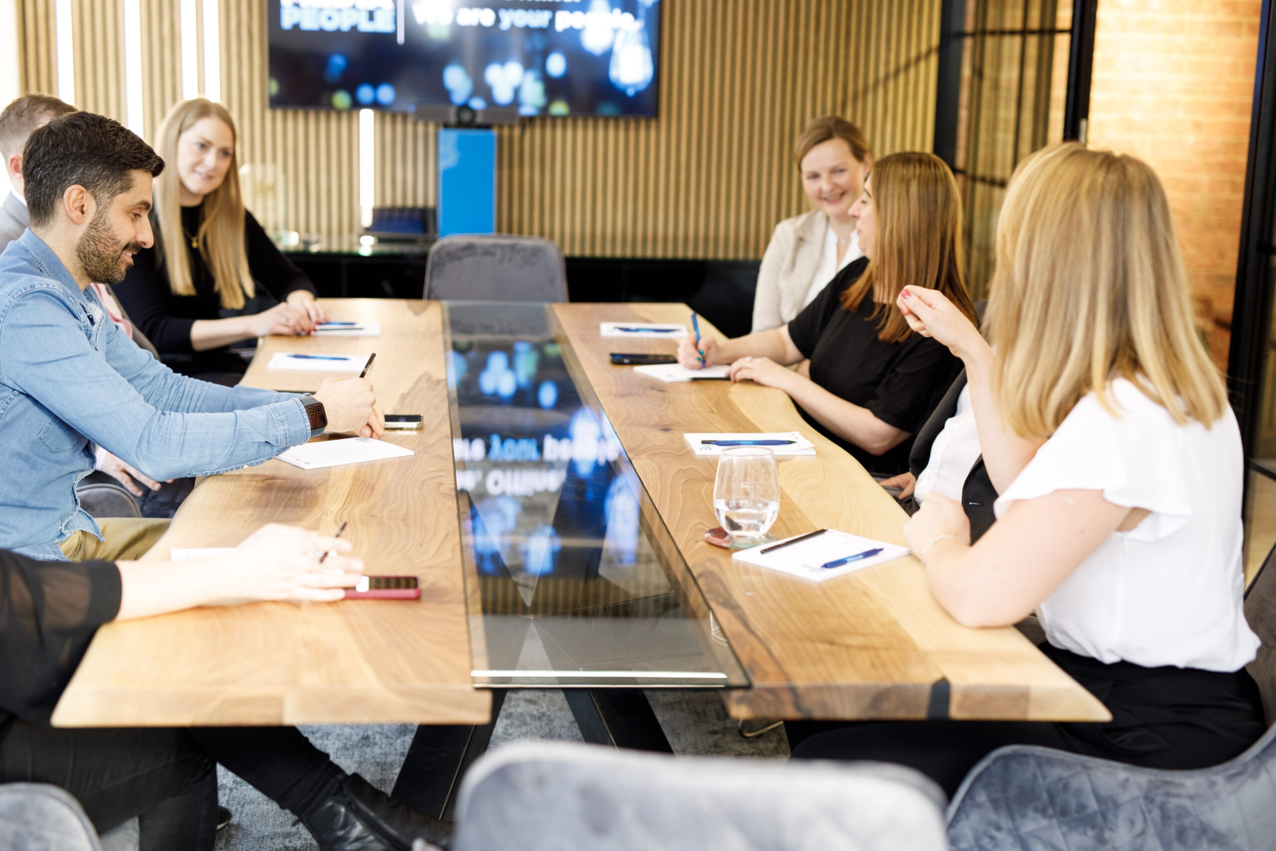 Six colleagues in a meeting around a wooden and glass boardroom table at The Media People