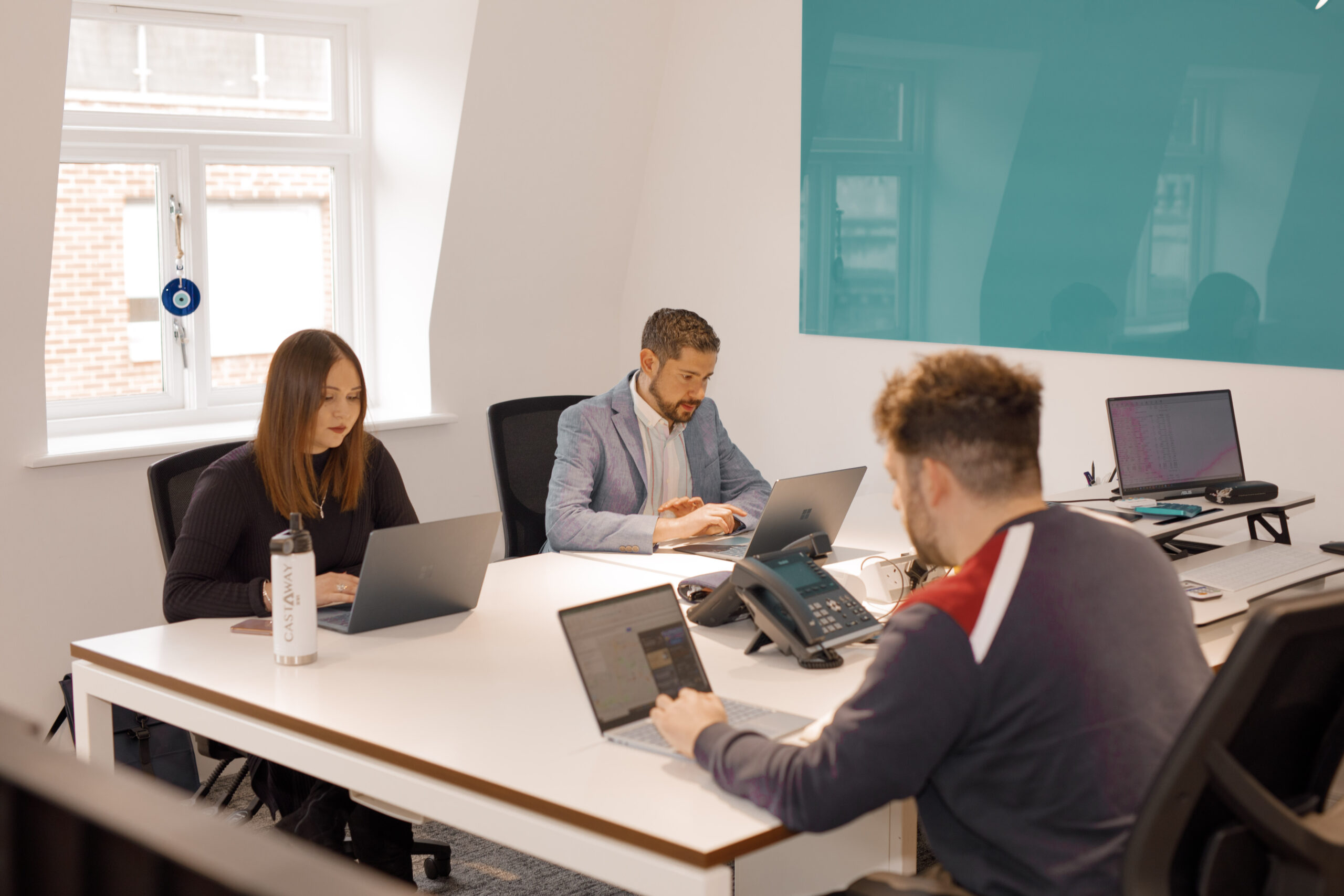 Three colleagues working on laptops at shared white desks in The Media People's office