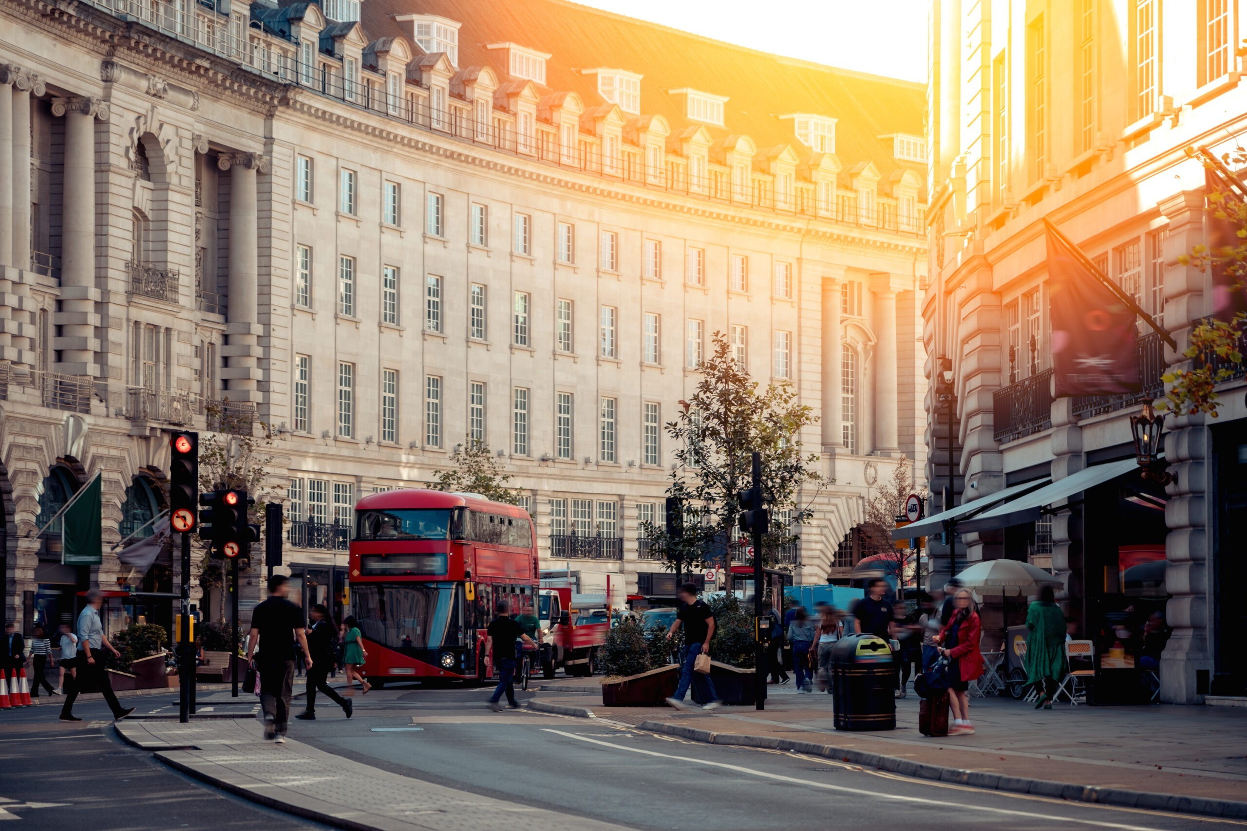 Shoppers and a red double-decker bus on a busy London street lined with grand stone buildings