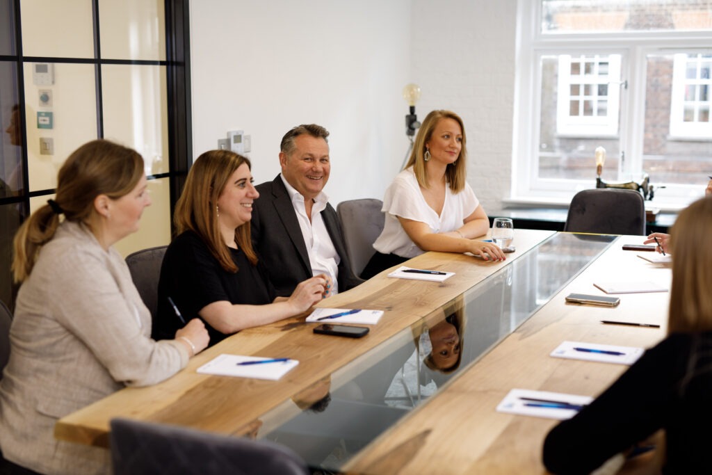 Colleagues smiling around a boardroom table with notepads in The Media People's bright meeting room