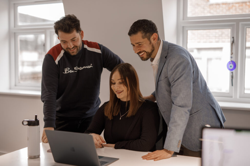 Three colleagues smiling at a laptop together in a bright office at The Media People