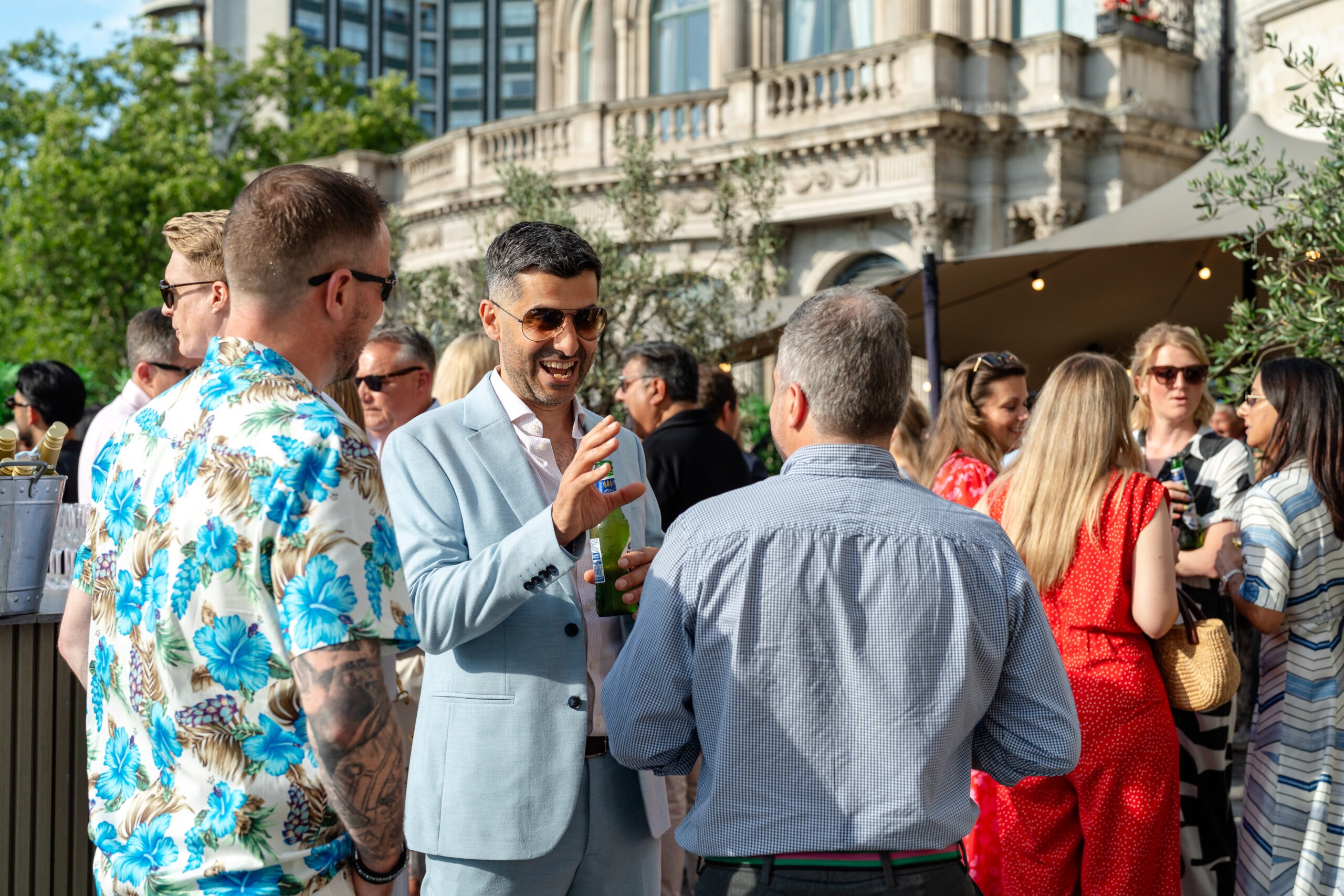 Guests laughing and talking with drinks by a stone building at The Media People's summer event